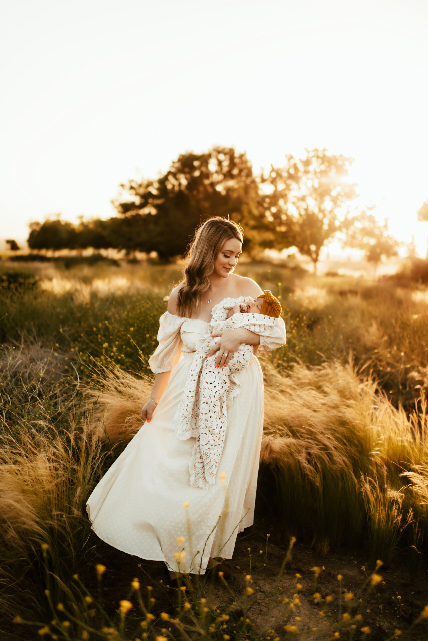 Mother looking lovingly at her baby in a field at sunset while swaying her dress